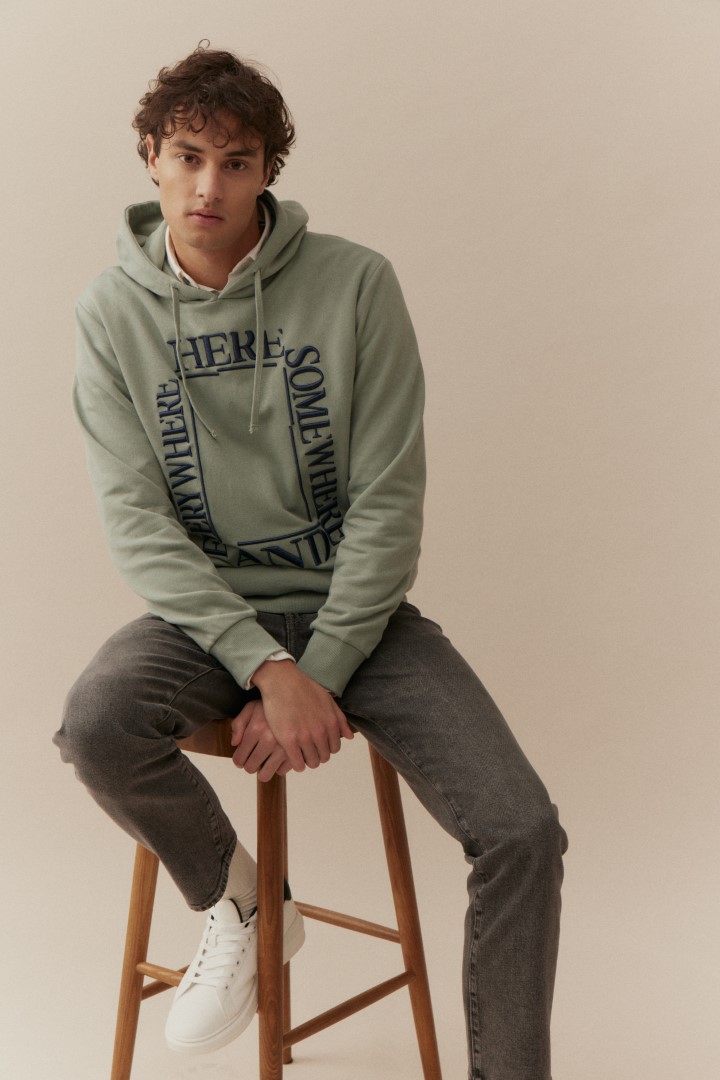 Basefield Men Model sitzt auf Stuhl und trägt Hoodie