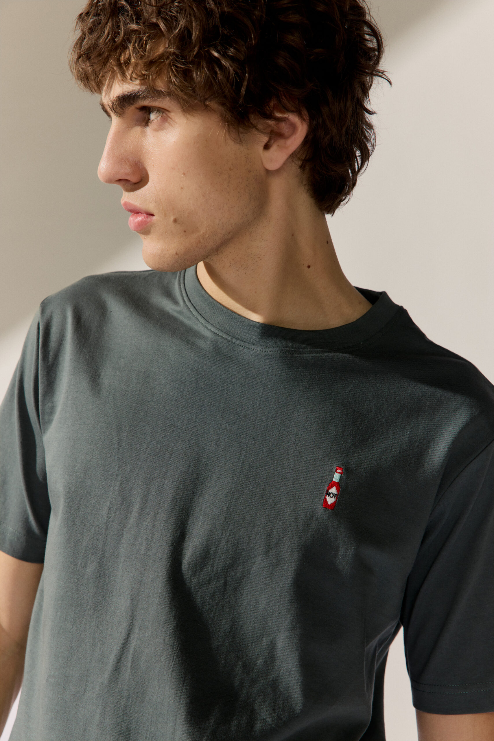 Basefield Men Model trägt T-Shirt in olive mit Schriftzug non parlo italiano und hat eine Tasche in der Hand