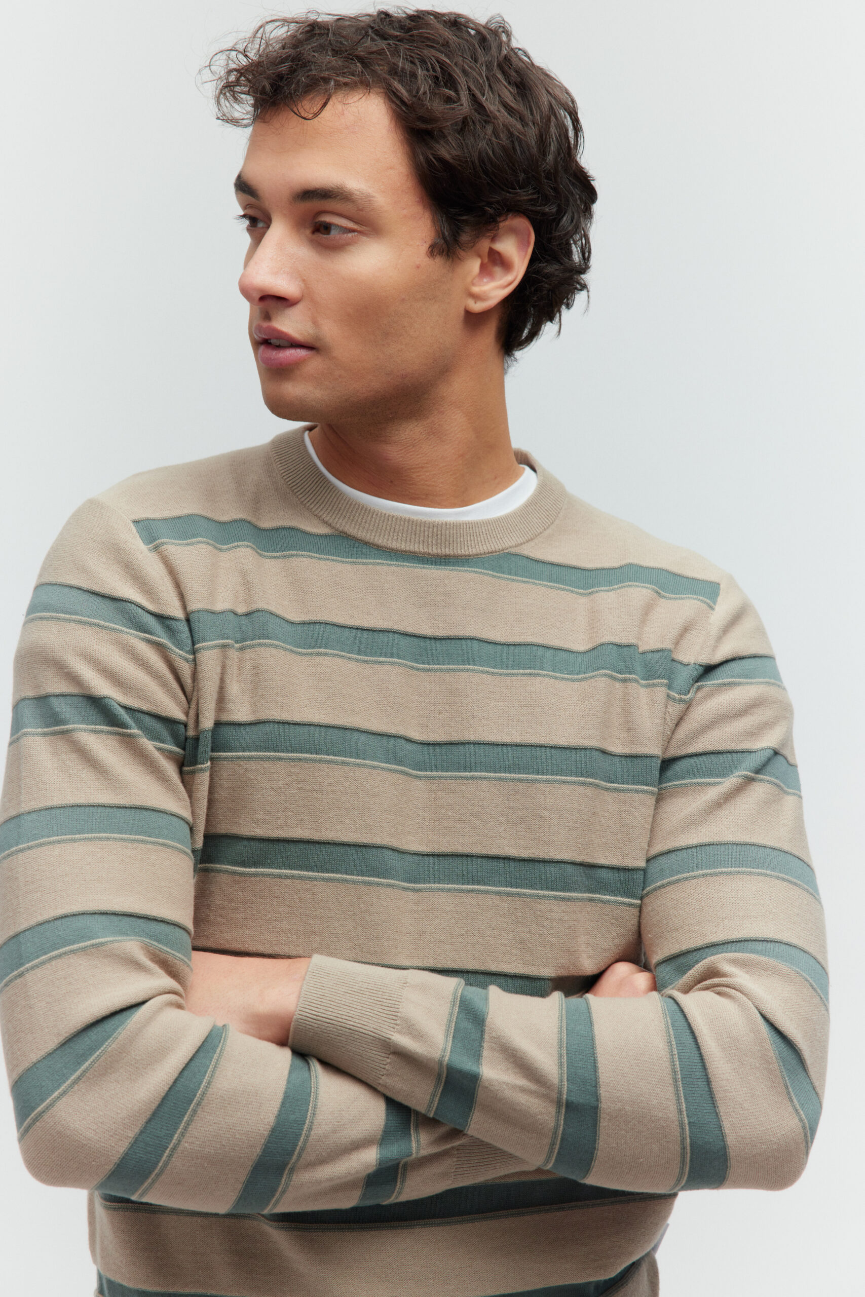 Porträt eines Models im beige-grün gestreiften Pullover, die Arme vor der Brust verschränkt.