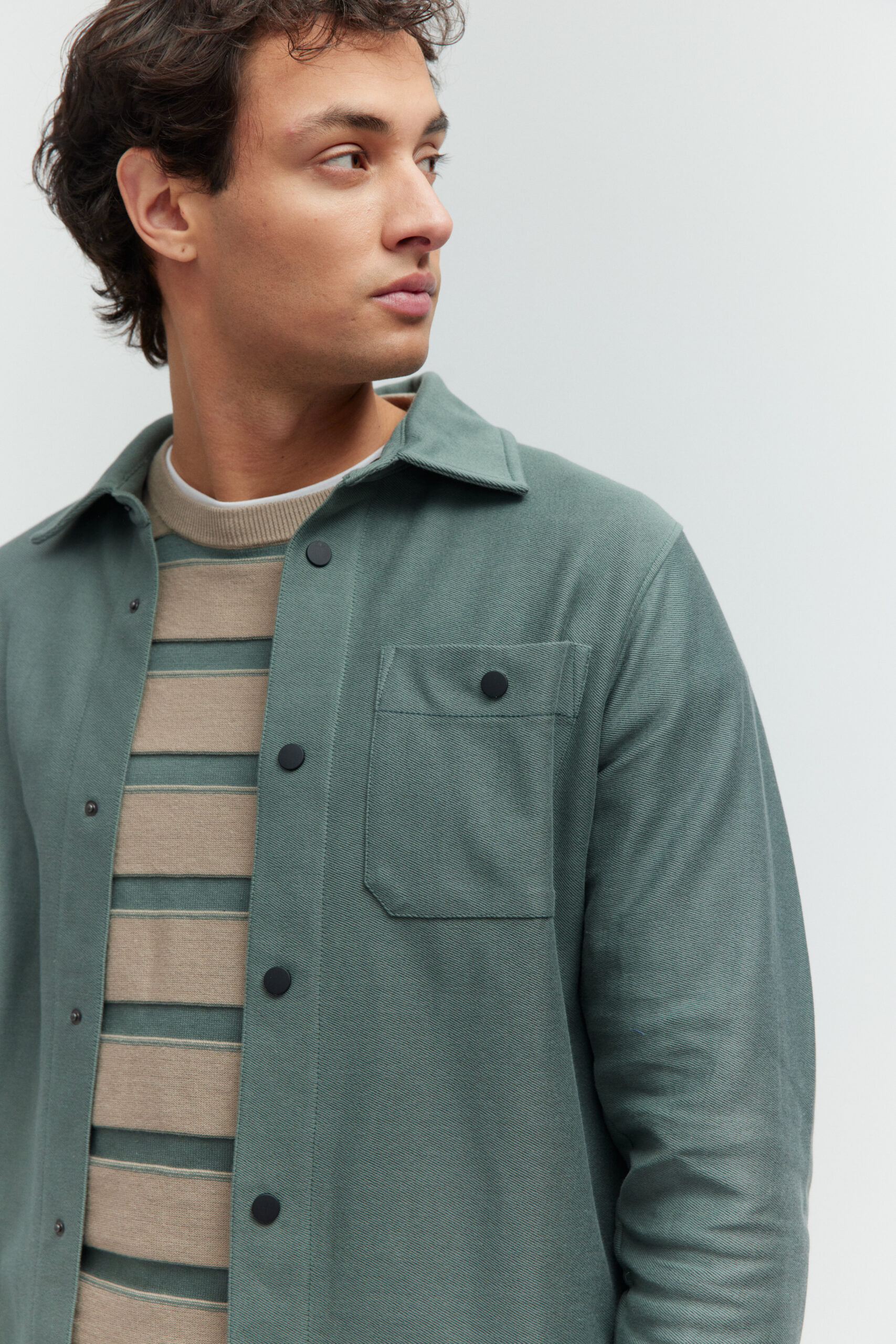 Model in grünem Overshirt über einem beige-grün gestreiften Pullover.