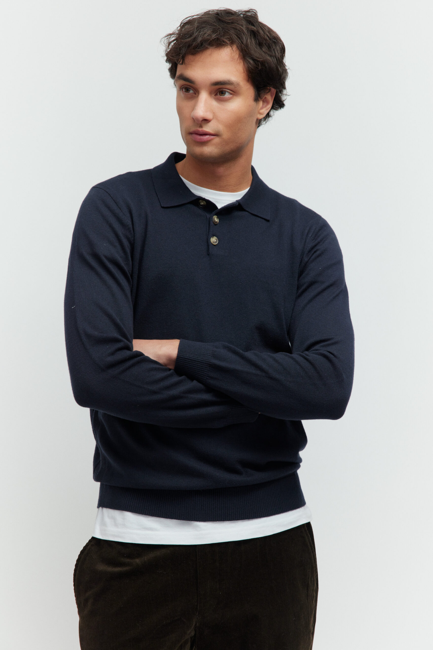Model in dunkelblauem Langarm-Poloshirt und dunkler Hose, die Arme vor der Brust verschränkt.