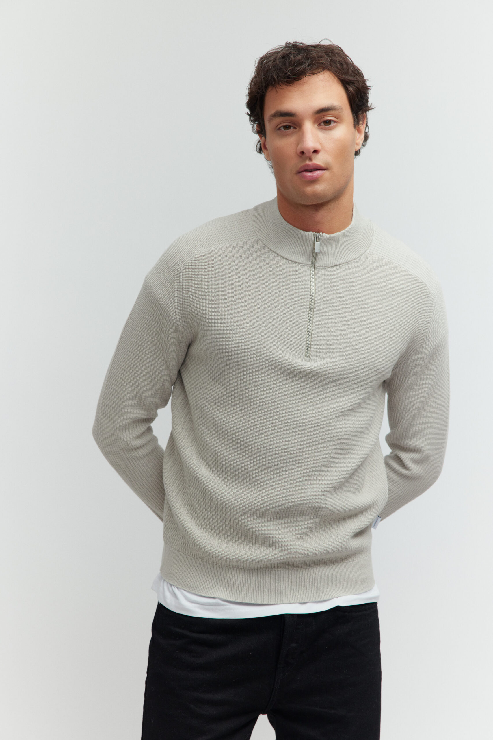 Model in hellgrauem Pullover mit Reißverschluss vor hellem Hintergrund.